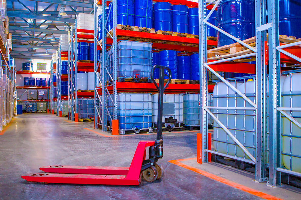 Image of bulk drums of chemicals and hazardous materials in a warehouse with a forklift. 