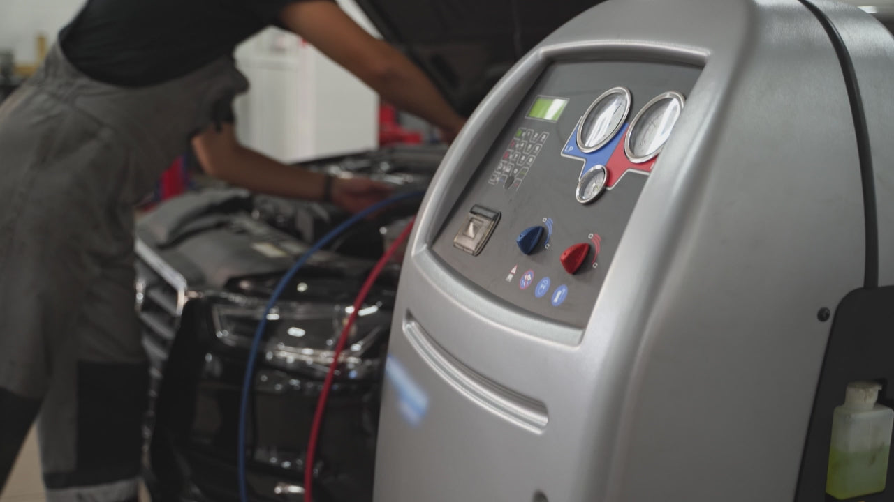 Auto mechanic refills refrigerant in car AC system.